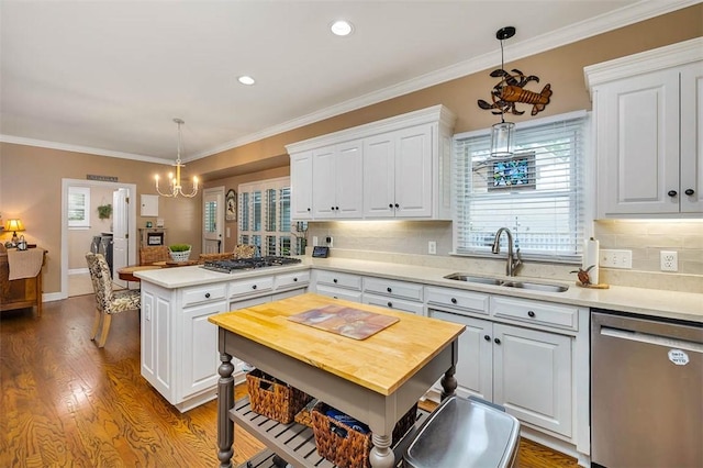 kitchen featuring appliances with stainless steel finishes, a sink, a peninsula, white cabinets, and backsplash