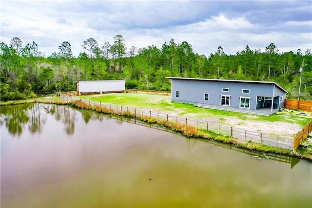 exterior space with an outbuilding, a water view, fence, and a view of trees