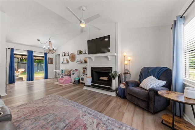 living room with ceiling fan with notable chandelier, wood finished floors, lofted ceiling, and a fireplace