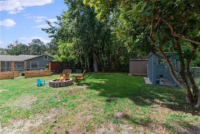 view of yard featuring a storage shed, fence, an outdoor structure, and a fire pit