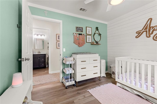 bedroom with ceiling fan, visible vents, wood walls, wood finished floors, and a crib