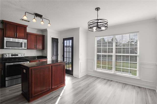 kitchen with appliances with stainless steel finishes, a textured ceiling, an inviting chandelier, light hardwood / wood-style flooring, and a kitchen island