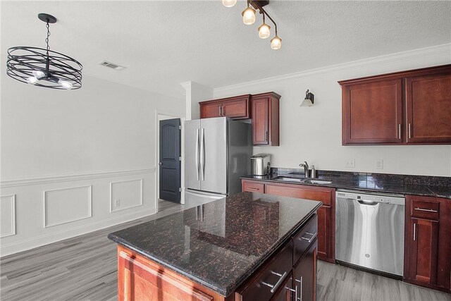 kitchen with appliances with stainless steel finishes, sink, light hardwood / wood-style flooring, a notable chandelier, and a center island