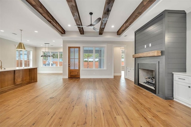 unfurnished living room with light wood finished floors, a large fireplace, baseboards, and ceiling fan