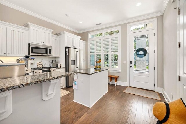 kitchen featuring white cabinetry, dark hardwood / wood-style flooring, dark stone counters, a kitchen island, and appliances with stainless steel finishes