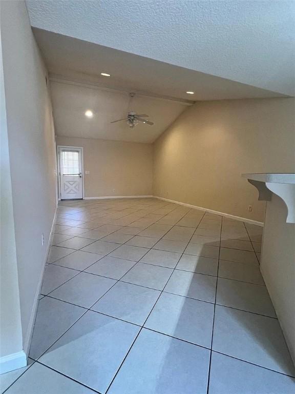 tiled spare room featuring ceiling fan, a textured ceiling, and vaulted ceiling