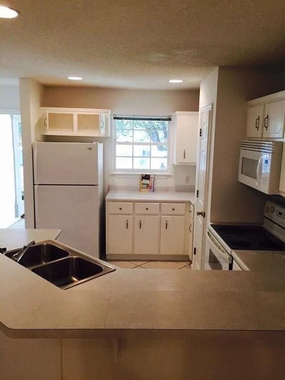 kitchen with a textured ceiling, white cabinetry, white appliances, and sink