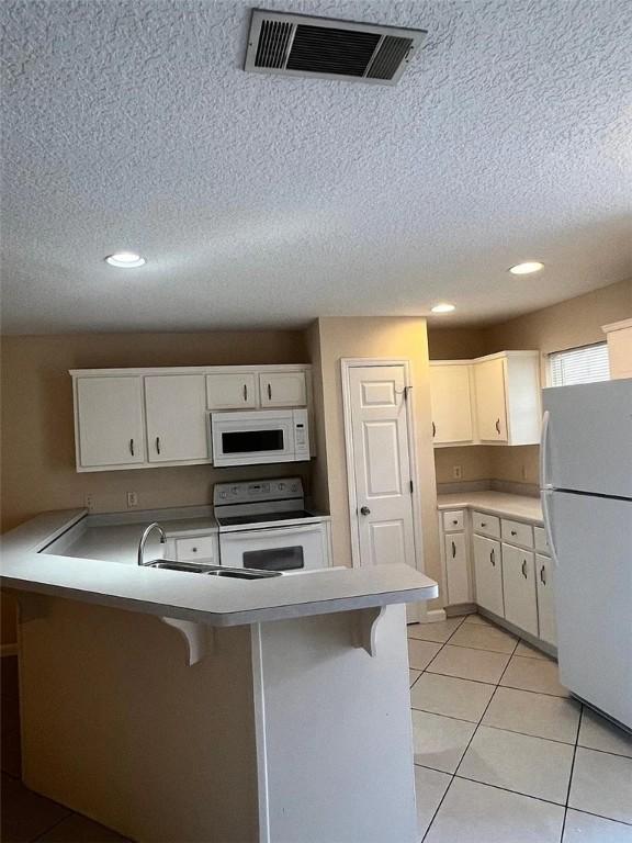 kitchen featuring white cabinets, white appliances, kitchen peninsula, and a breakfast bar area