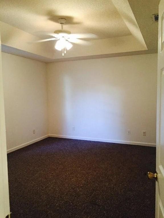 spare room with a textured ceiling, carpet floors, a tray ceiling, and ceiling fan