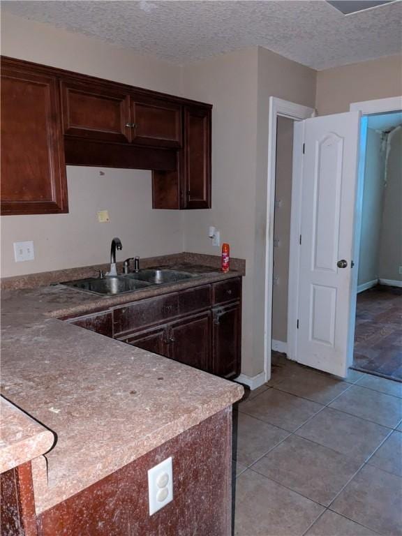 kitchen featuring a textured ceiling, dark brown cabinets, light tile patterned flooring, and sink