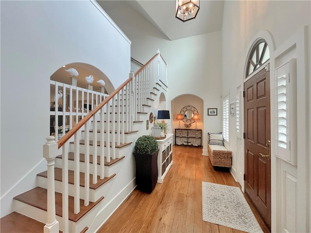 entrance foyer featuring stairway, a towering ceiling, an inviting chandelier, and wood finished floors