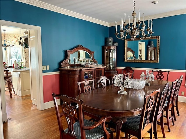 dining area with sink, light wood-type flooring, crown molding, and an inviting chandelier