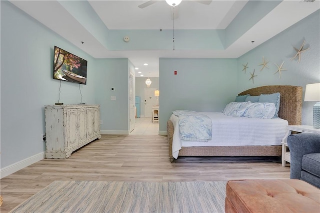 bedroom featuring baseboards, light wood-style floors, and a tray ceiling