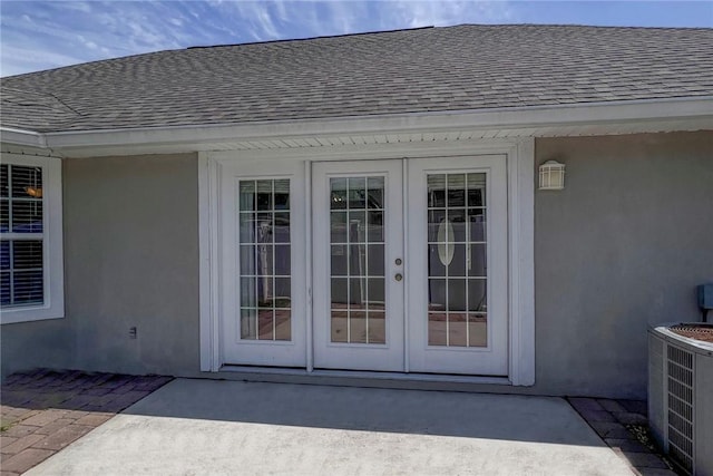entrance to property featuring french doors, central air condition unit, a shingled roof, and stucco siding