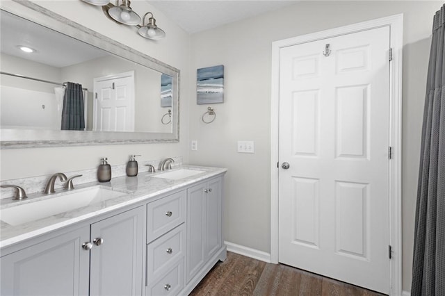 bathroom featuring double vanity, baseboards, a sink, and wood finished floors
