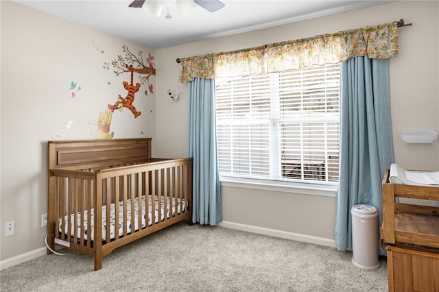 bedroom with a crib, baseboards, a ceiling fan, and carpet flooring