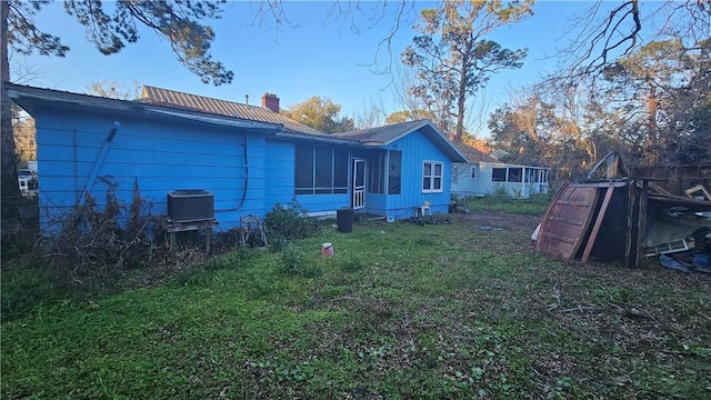 rear view of house featuring metal roof, a yard, and a chimney