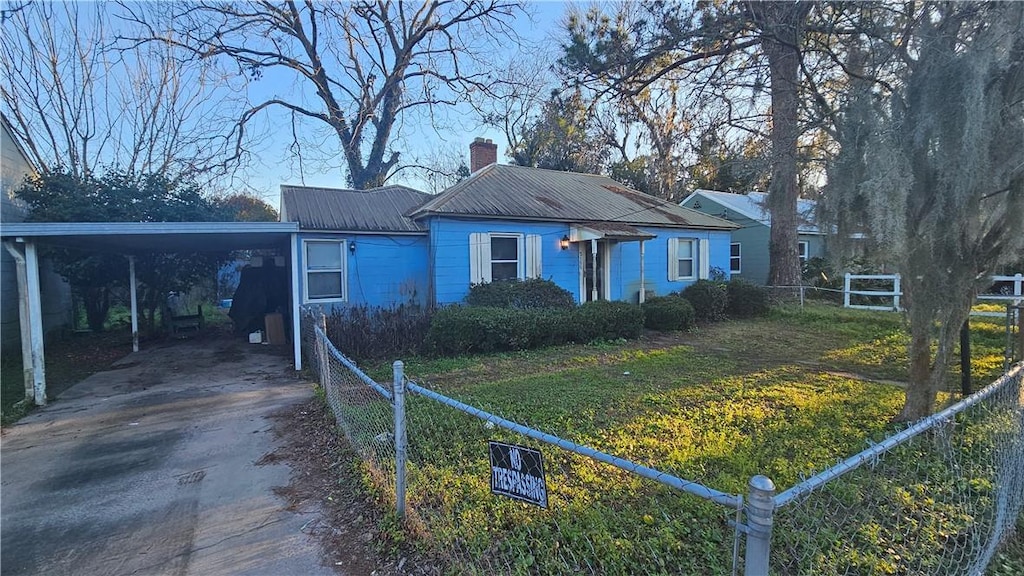bungalow-style house featuring metal roof, fence, an attached carport, driveway, and a front lawn