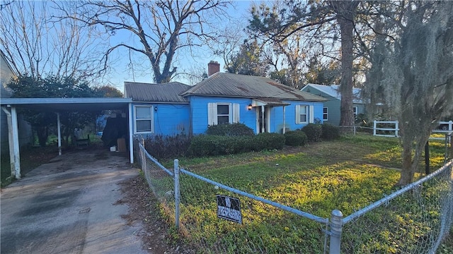 bungalow-style house featuring metal roof, fence, an attached carport, driveway, and a front lawn