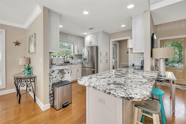 200 Colgana Way, Saint Simons Island, GA 31522 - kitchen with stainless steel fridge with ice dispenser, a peninsula, a kitchen breakfast bar, light wood-type flooring, and light stone countertops