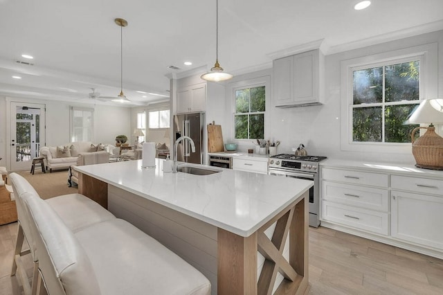 kitchen featuring pendant lighting, white cabinetry, an island with sink, sink, and stainless steel appliances