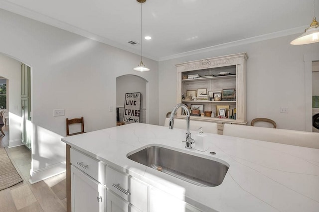 kitchen featuring sink, white cabinetry, light stone counters, decorative light fixtures, and light wood-type flooring