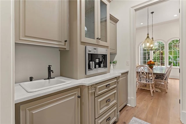 kitchen with light stone countertops, sink, pendant lighting, and light hardwood / wood-style flooring