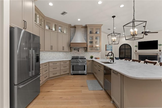 kitchen featuring sink, hanging light fixtures, stainless steel appliances, custom range hood, and light wood-type flooring