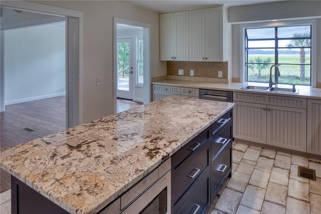 kitchen featuring light stone countertops, sink, light hardwood / wood-style flooring, decorative backsplash, and a kitchen island