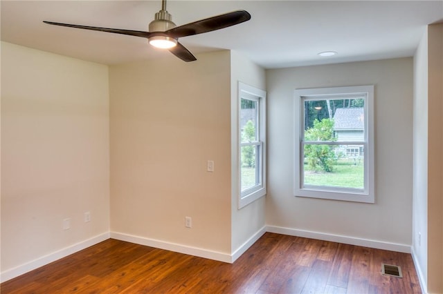 empty room with dark wood-style flooring, visible vents, ceiling fan, and baseboards