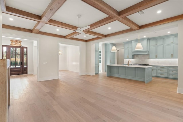 kitchen featuring decorative light fixtures, an island with sink, decorative backsplash, coffered ceiling, and light wood-type flooring