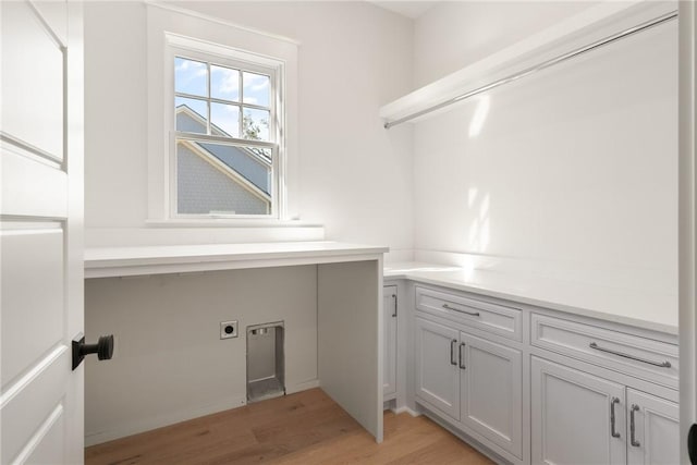 laundry room with electric dryer hookup, light hardwood / wood-style flooring, and cabinets