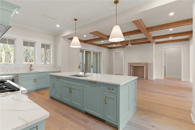 kitchen with sink, light hardwood / wood-style floors, hanging light fixtures, and a center island with sink