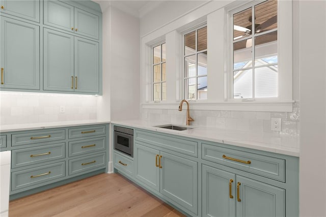 kitchen with stainless steel microwave, sink, tasteful backsplash, and light wood-type flooring