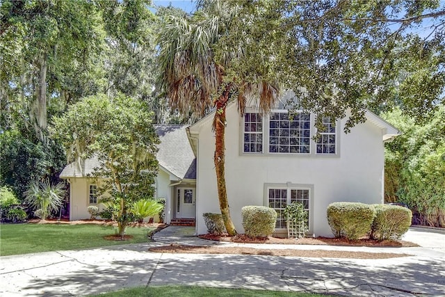 view of front facade with a front lawn, a shingled roof, and stucco siding