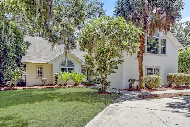 view of front of property featuring a shingled roof, a front yard, and stucco siding