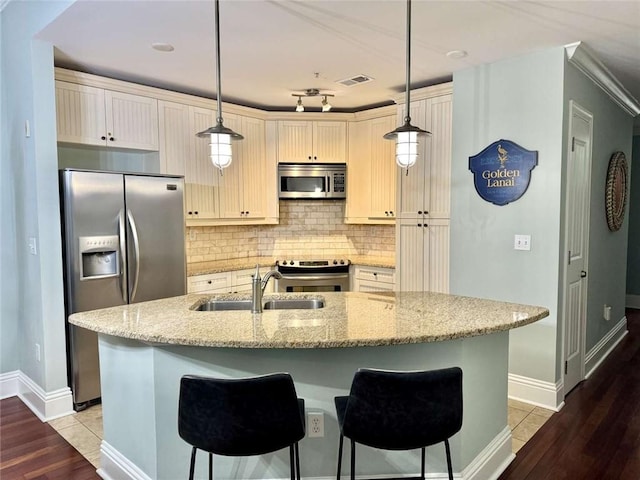 kitchen with sink, hanging light fixtures, appliances with stainless steel finishes, light stone counters, and wood-type flooring