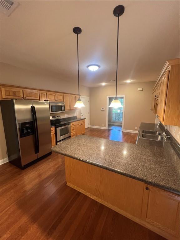 134 Hillery Trce, Brunswick, GA 31523 - kitchen featuring appliances with stainless steel finishes, dark wood-style flooring, a peninsula, decorative light fixtures, and dark stone counters