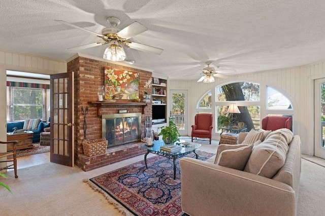 carpeted living room featuring ceiling fan, ornamental molding, a textured ceiling, a brick fireplace, and wood walls