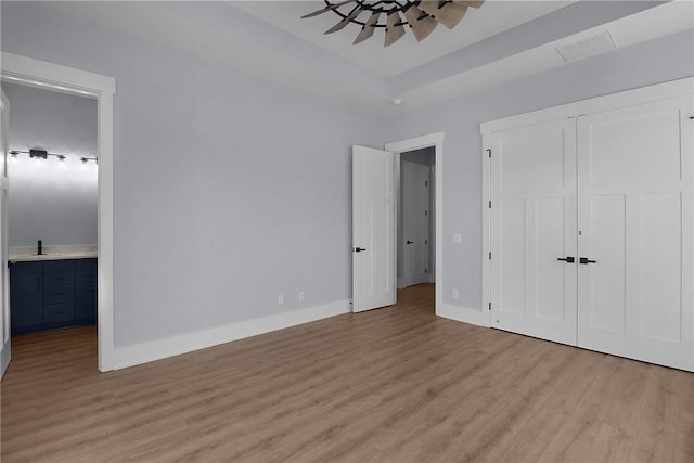 unfurnished bedroom with ensuite bath, baseboards, light wood-type flooring, and a closet