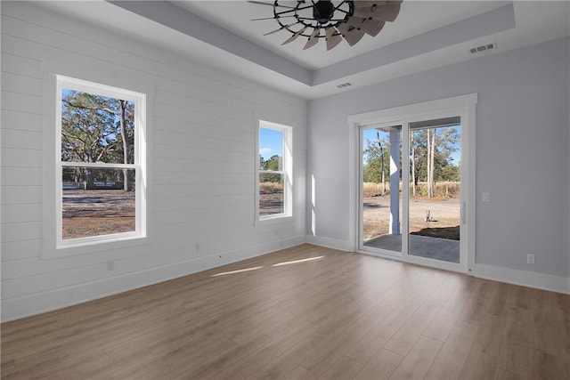 empty room featuring visible vents, a raised ceiling, baseboards, and wood finished floors