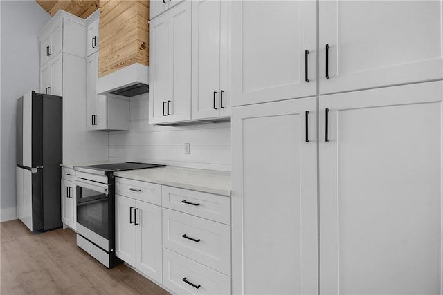 kitchen with light wood-type flooring, light countertops, electric range oven, freestanding refrigerator, and white cabinets