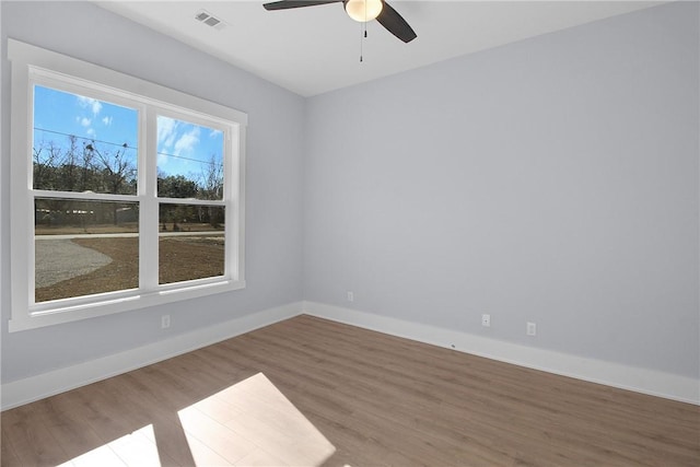 empty room with a ceiling fan, wood finished floors, visible vents, and baseboards