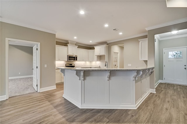154 Ossabaw Way, Waverly, GA 31565 - kitchen featuring appliances with stainless steel finishes, a kitchen bar, light wood-type flooring, crown molding, and white cabinetry