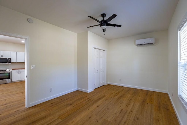 spare room with baseboards, a wall unit AC, light wood-style floors, and ceiling fan