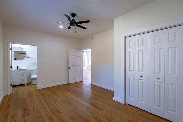 unfurnished bedroom with a closet, ensuite bathroom, baseboards, and wood finished floors