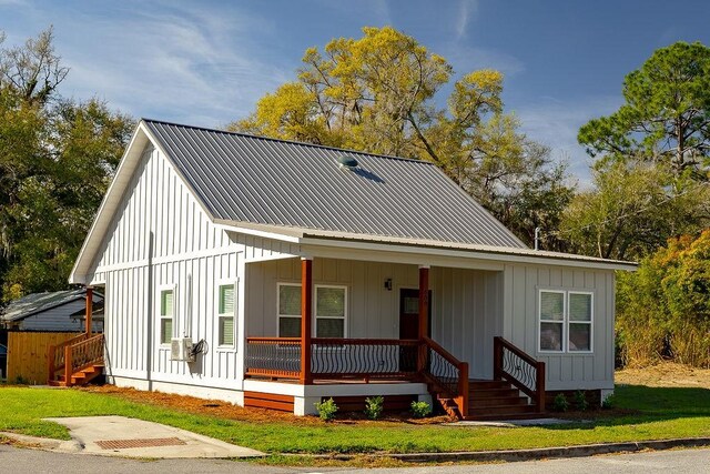 modern inspired farmhouse with covered porch, metal roof, board and batten siding, and a front yard