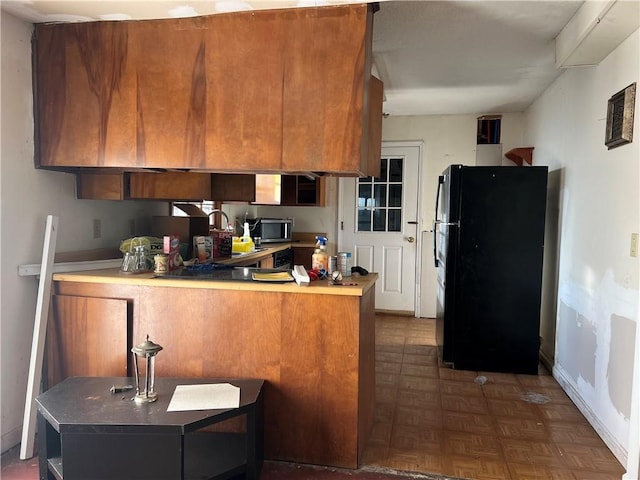 kitchen featuring dark parquet flooring, kitchen peninsula, and black refrigerator