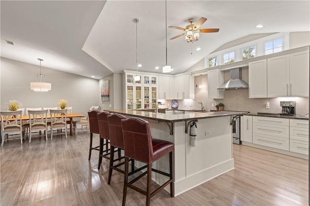 636 Old Plantation Rd, Jekyll Island, GA 31527 - kitchen featuring wall chimney range hood, a sink, lofted ceiling, a breakfast bar area, and light wood finished floors