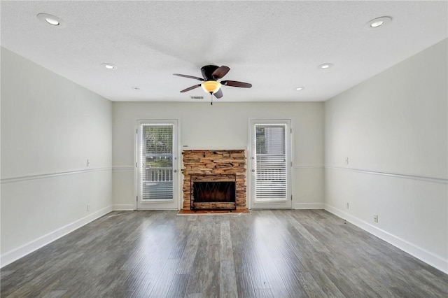 unfurnished living room with a textured ceiling, dark hardwood / wood-style floors, a stone fireplace, and ceiling fan